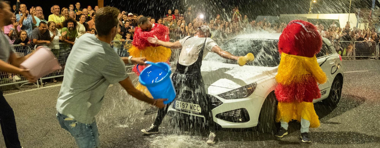 Spectacle de clown et rue passé par l'eau d’Agro the Clown... Car Wash. Agro le clown recevant un seau d'eau d'un spectateur à côté d'une voiture entourée de public. Luca Della Gatta