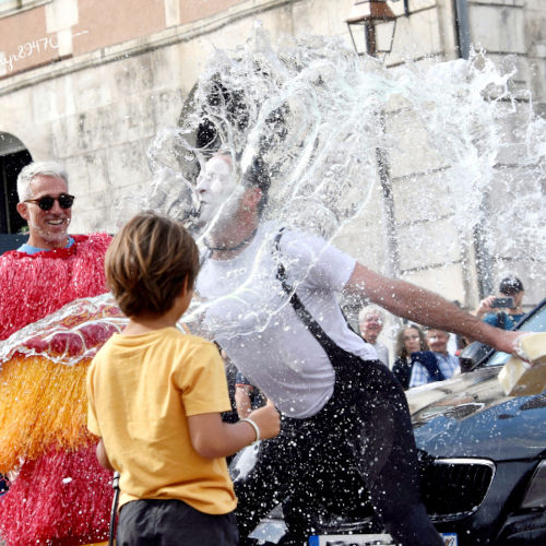 Luca Della Gatta.Car Wash Spectacle de clown et rue. Agro the clown recevant un seau d'eau entouré par le public. Luca Della Gatta